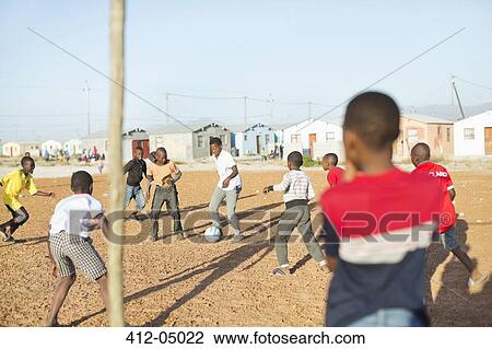 Stock Image - Boys playing soccer together in dirt field. Fotosearch