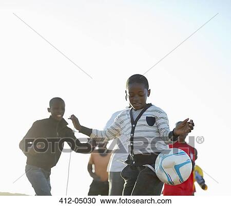 Stock Image - Boys playing soccer together in dirt field. Fotosearch