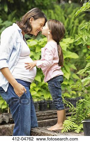 Stock Image - Girl kissing pregnant mother outdoors. Fotosearch