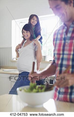 Stock Image - Pregnant mother and daughter watching father toss salad. Fotosearch