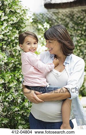 Picture - Pregnant mother holding daughter outdoors. Fotosearch