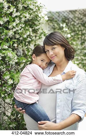 Picture - Pregnant mother holding daughter outdoors. Fotosearch