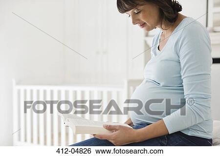 Stock Photograph - Pregnant woman reading in nursery. Fotosearch