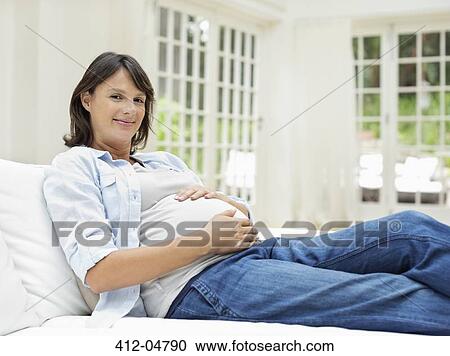 Stock Image - Pregnant woman relaxing on sofa. Fotosearch