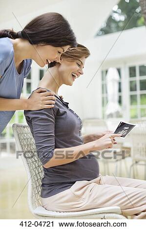 Stock Image - Pregnant woman showing friend sonogram. Fotosearch