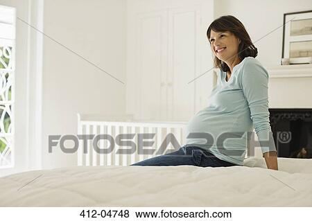 Stock Photo - Pregnant woman sitting on bed. Fotosearch