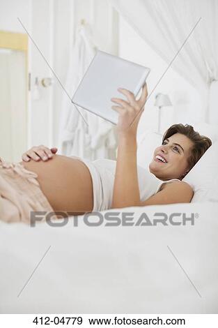Stock Photo - Pregnant woman using tablet computer on bed. Fotosearch