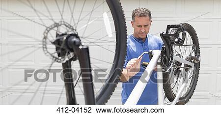 Stock Image - Man working on bicycle in driveway. Fotosearch