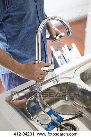 Stock Image - Plumber working on kitchen sink. Fotosearch