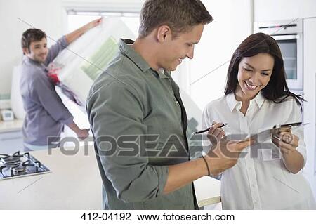 Stock Image - Woman signing for delivery in kitchen. Fotosearch