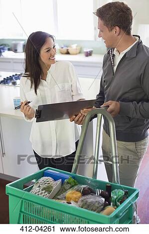 Stock Image - Woman signing for delivery in kitchen. Fotosearch