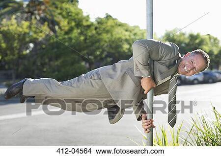Picture - Businessman balancing on pole on city street. Fotosearch