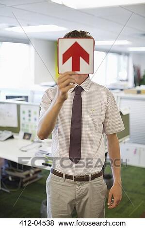 Businessman holding arrow sign in office View Large Photo Image Stock Photo - Businessman holding arrow sign in office. Fotosearch