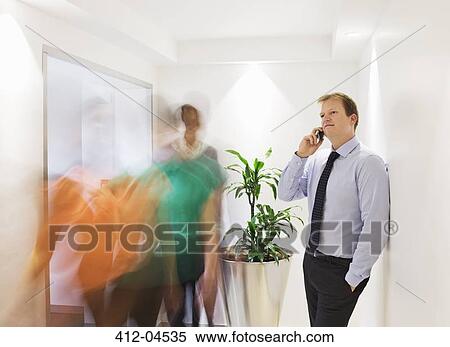 Businessman on cell phone in busy hallway View Large Photo Image Stock Photography - Businessman on cell phone in busy hallway. Fotosearch