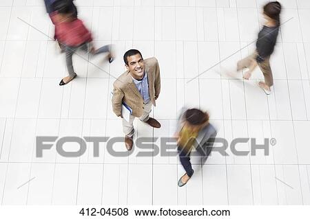 Businessman smiling in busy office hallway View Large Photo Image Stock Photo - Businessman smiling in busy office hallway. Fotosearch