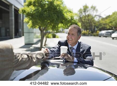 Stock Image - Businessmen shaking hands over car. Fotosearch