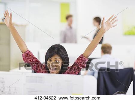 Stock Image - Businesswoman cheering at desk. Fotosearch