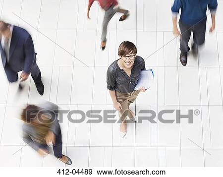 Stock Photo - Businesswoman smiling in busy office hallway. Fotosearch