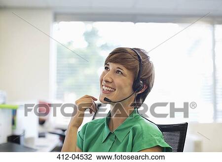 Stock Image - Businesswoman talking on headset at desk. Fotosearch