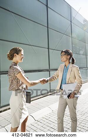 Stock Image - Businesswomen shaking hands on city street. Fotosearch
