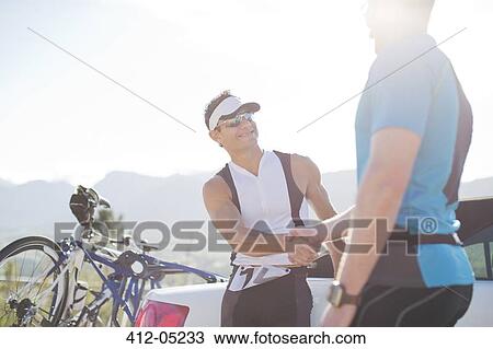 Stock Image - Cyclists shaking hands on rural road. Fotosearch