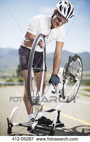 Man adjusting bicycle on rural road View Large Photo Image Stock Photo - Man adjusting bicycle on rural road. Fotosearch