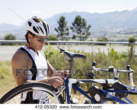 Stock Image - Man adjusting bicycle outdoors. Fotosearch