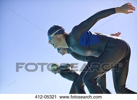 Stock Image - Triathletes diving into water outdoors. Fotosearch