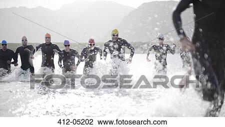 Stock Image - Triathletes in wetsuits running in waves. Fotosearch