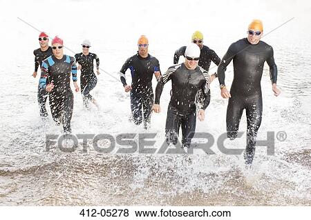 Triathletes in wetsuits running in waves View Large Photo Image Stock Photo - Triathletes in wetsuits running in waves. Fotosearch