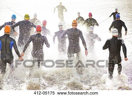 Stock Photography - Triathletes in wetsuits running into ocean. Fotosearch