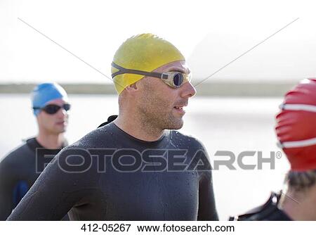 Stock Photo - Triathletes in wetsuits standing on beach. Fotosearch