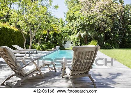 Stock Photograph - Lawn chairs and swimming pool in backyard. Fotosearch