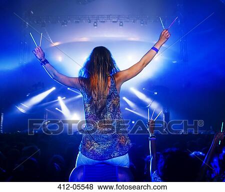 Stock Photo - Cheering woman with glow sticks on man's shoulders at music festival. Fotosearch