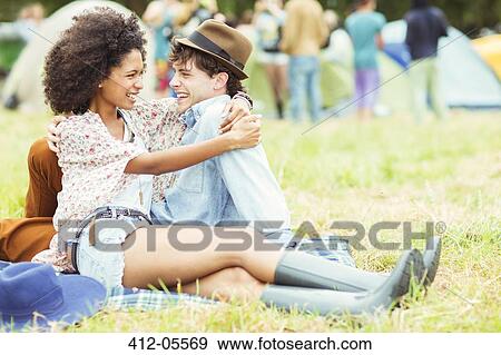 Stock Photo - Couple hugging in grass outside tents at music festival. Fotosearch