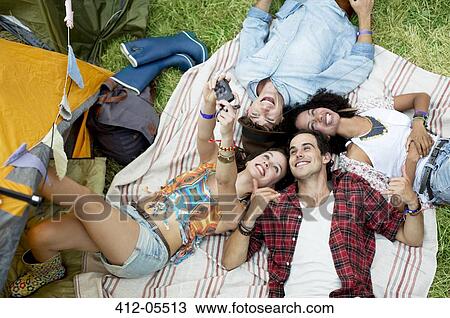 Stock Image - Friends taking self-portrait on blanket outside tent at music festival. Fotosearch