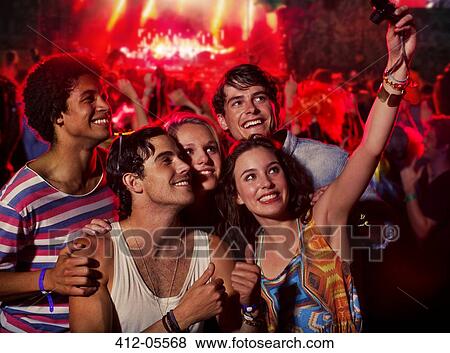 Stock Photo - Friends taking self-portrait with camera phone at music festival. Fotosearch