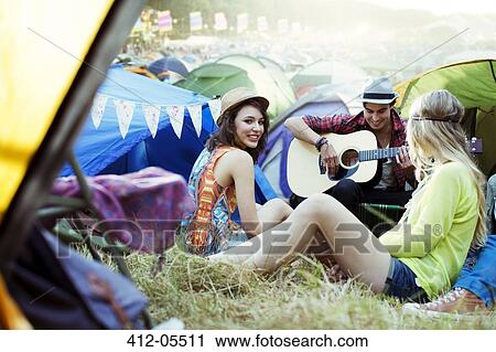 Stock Image - Friends with guitar hanging out near tents at music festival. Fotosearch