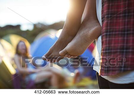Stock Image - Man carrying barefoot woman outside tents at music festival. Fotosearch