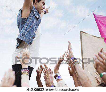 Stock Image - Performer standing above cheering crowd at music festival. Fotosearch