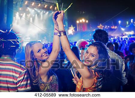 Stock Photo - Portrait of cheering women with glow sticks at music festival. Fotosearch