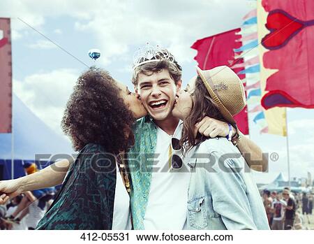 Stock Image - Women kissing man's cheek at music festival. Fotosearch