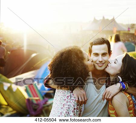 Picture - Women kissing man's cheek outside tents at music festival. Fotosearch