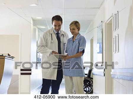 Stock Image - Doctor and nurse using tablet computer in hospital hallway. Fotosearch