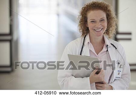 Stock Image - Doctor carrying clipboard in hospital hallway. Fotosearch
