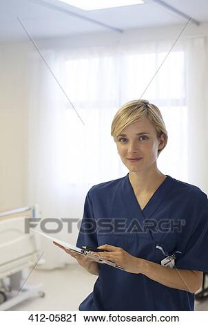 Stock Image - Nurse reading clipboard in hospital hallway. Fotosearch