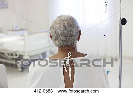 Stock Image - Older patient wearing gown in hospital room. Fotosearch