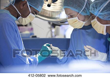 Stock Image - Surgeons bent over patient on operating table. Fotosearch