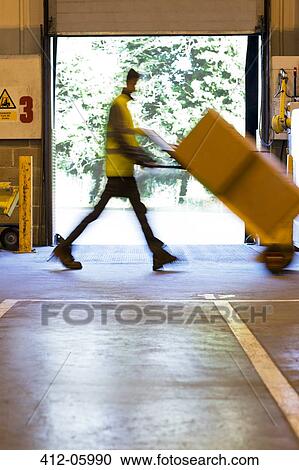 Stock Image - Blurred view of worker carting boxes in warehouse. Fotosearch