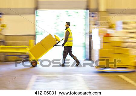 Stock Image - Blurred view of worker pushing boxes in warehouse. Fotosearch